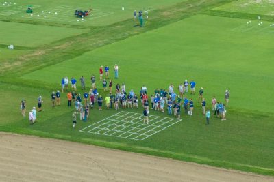 Aerial view of a turfgrass field demonstration. A crowd of people are standing around a white grid in the middle of a green lawn